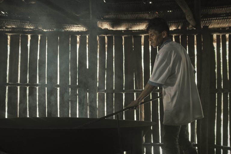 Al interior de la maloca, entre el humo y el calor, un hombre tuesta cuidadosamente las hojas de coca. El proceso es un acto de conocimiento y tradición, el primer paso para convertir la hoja en mambe, alimento espiritual y herramienta de la palabra. 20 de enero del 2025