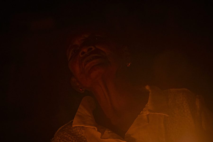 Abuela Matilde, reconocida sabia de la comunidad de San Pedro de los Lagos, participa en un ritual bajo la luz cálida del fuego. Su rostro emerge entre las sombras, iluminado por la intensidad del momento ceremonial.
Las abuelas sabedoras son guardianas de la memoria y la tradición. En ellas habita el conocimiento sobre la chagra, la yuca brava, los cantos y las medicinas que sostienen a sus pueblos. Su palabra transmite fuerza y continuidad; sus gestos encarnan la sabiduría femenina que asegura la vida. Cada enseñanza compartida es semilla para las nuevas generaciones, un legado que mantiene vivo el vínculo entre tierra, alimento y comunidad.